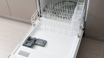 An open dishwasher with a detergent bottle and a cloth on the countertop above it.