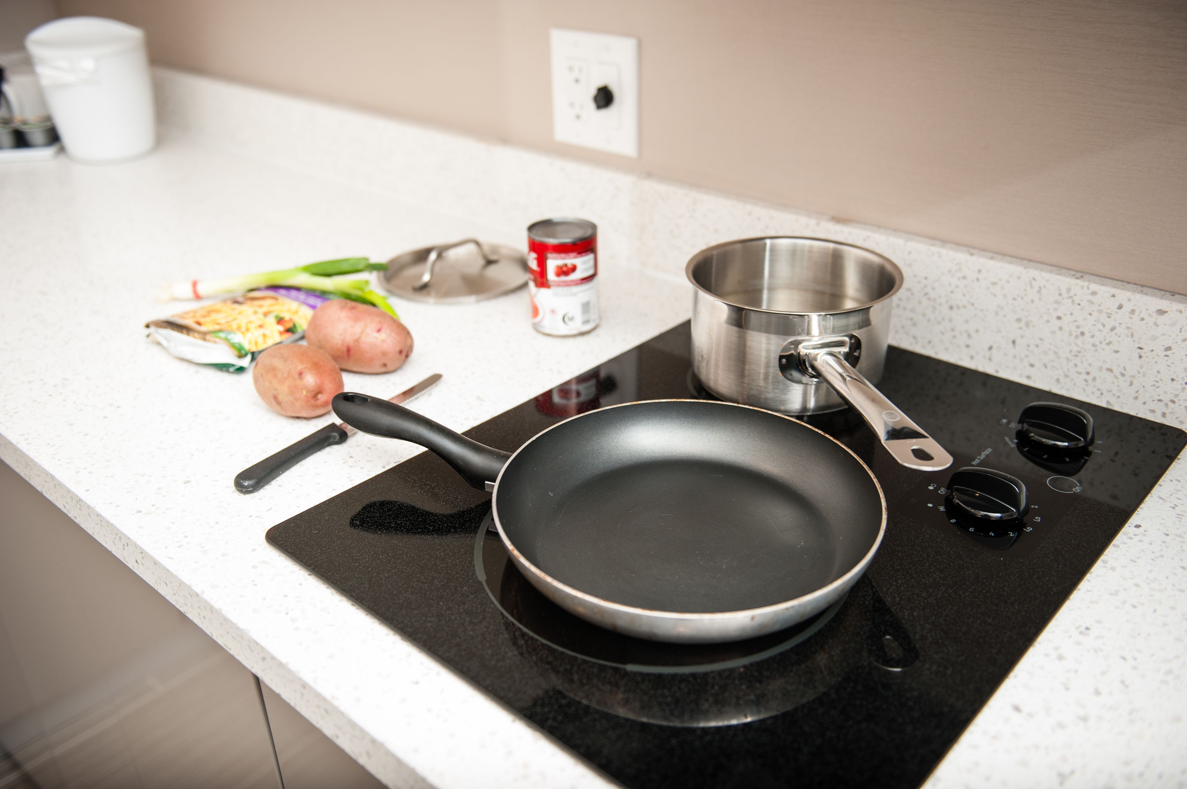 A kitchen counter with a frying pan, a pot, a can, and some vegetables.