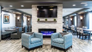 A modern lounge area with a flat-screen TV mounted on a stone wall, a fireplace, and seating arrangements including sofas and chairs.
