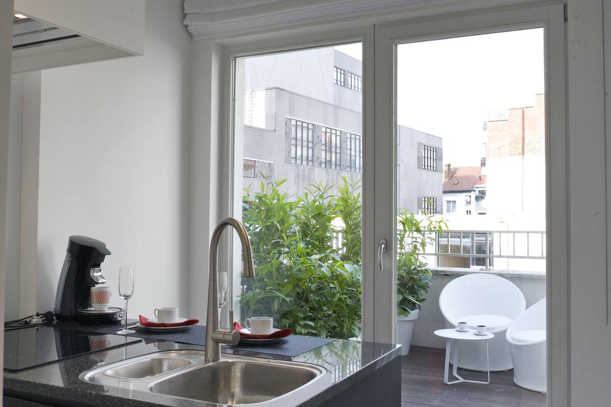 Una cocina moderna con encimera oscura, pileta doble y vistas a un balcón con mobiliario exterior.