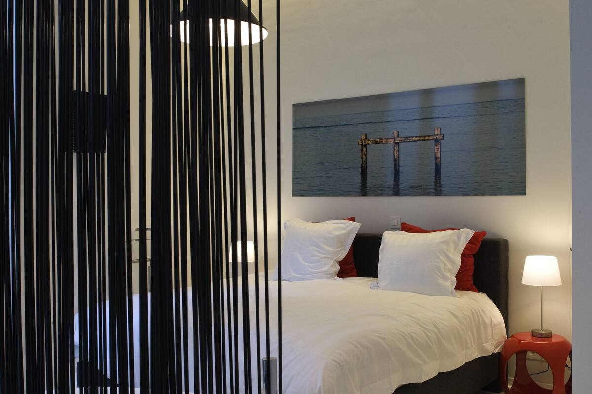Un dormitorio moderno con una cama, una mesita de noche roja y otra blanca, y un cuadro en la pared.