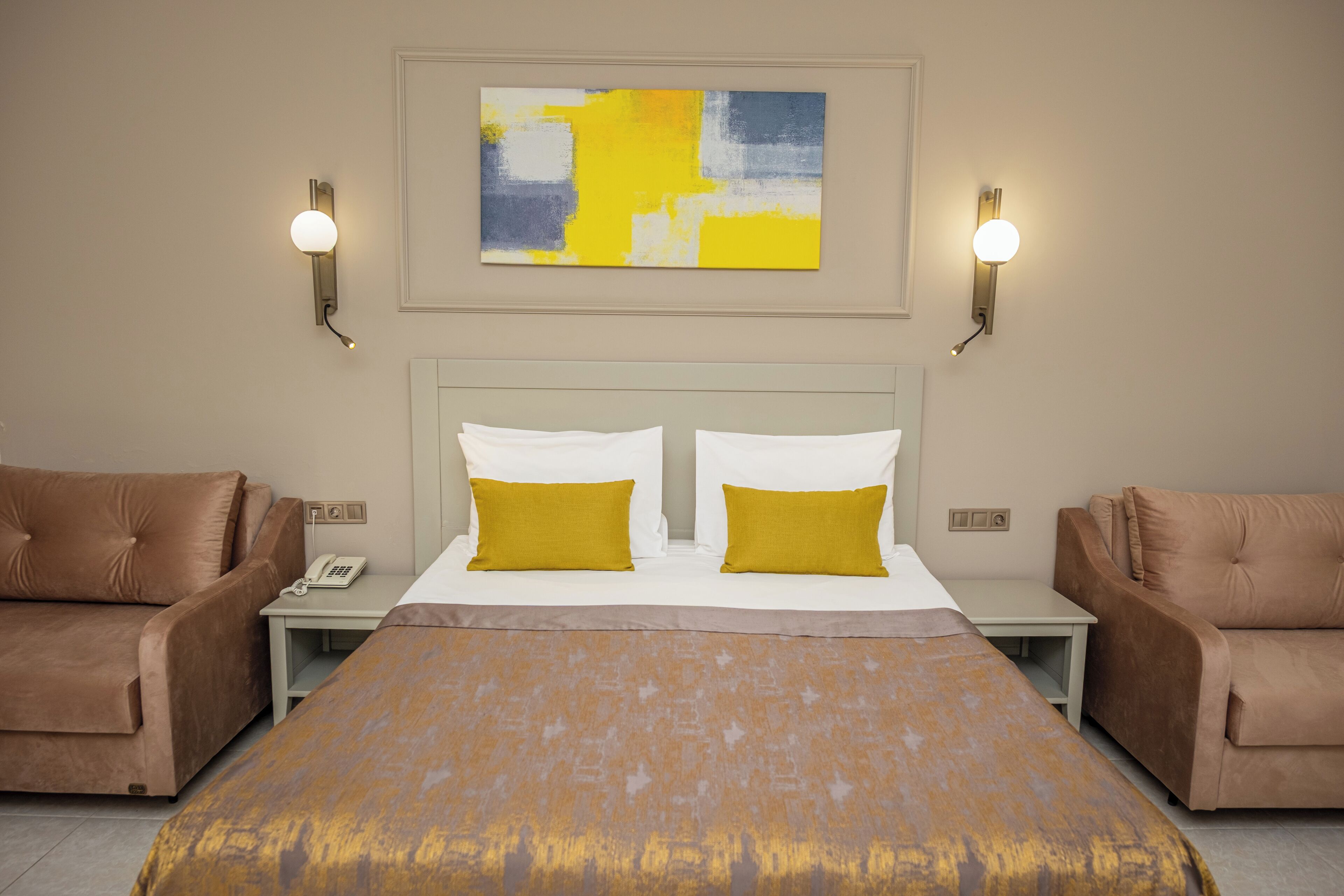 Una habitación de hotel con una cama grande, dos mesitas de noche, un teléfono y dos sillones marrones.