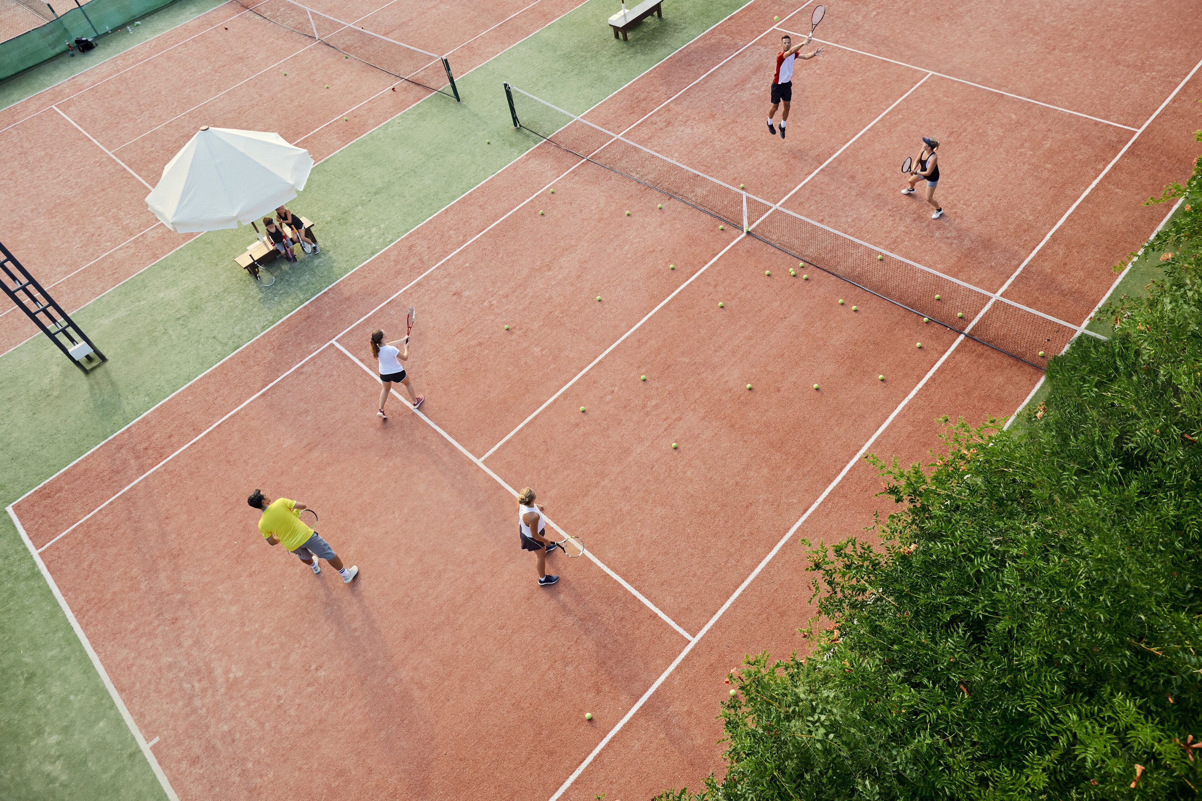Una cancha de tenis con varios jugadores, un banco y una sombrilla grande.