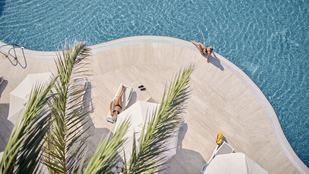 Zona de piscina con borde curvo, sillas de descanso y palmeras.
