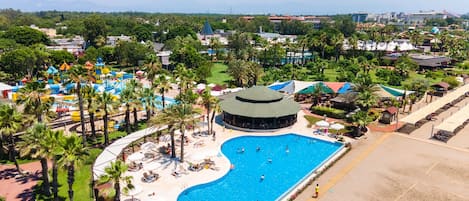 Vista aérea de un complejo turístico con una gran piscina, palmeras y varios edificios.