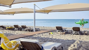 Zona de playa con sombrillas, sillas de descanso y una terraza de madera.