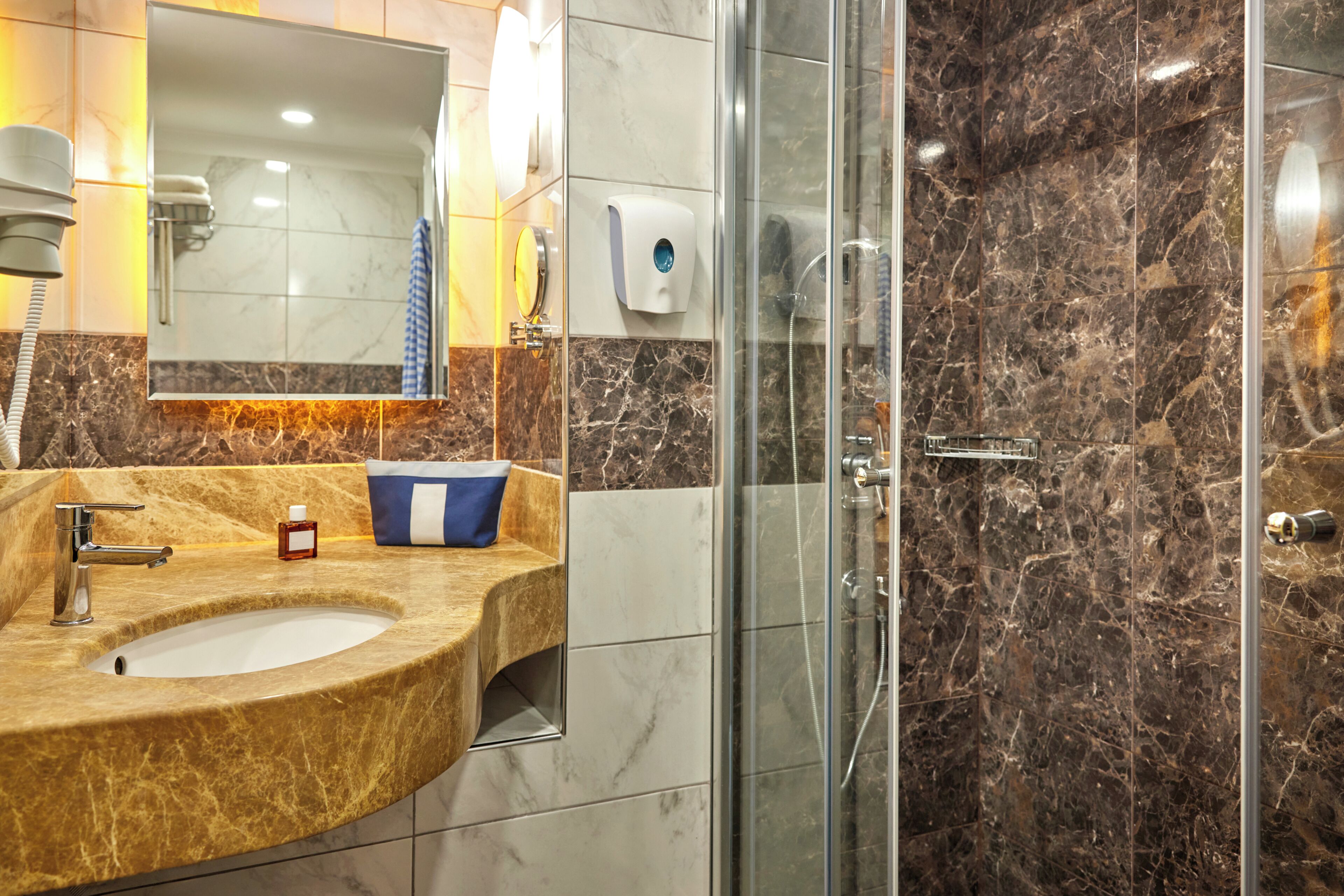 A bathroom with a marble sink, a glass shower enclosure, and a hand soap dispenser.
