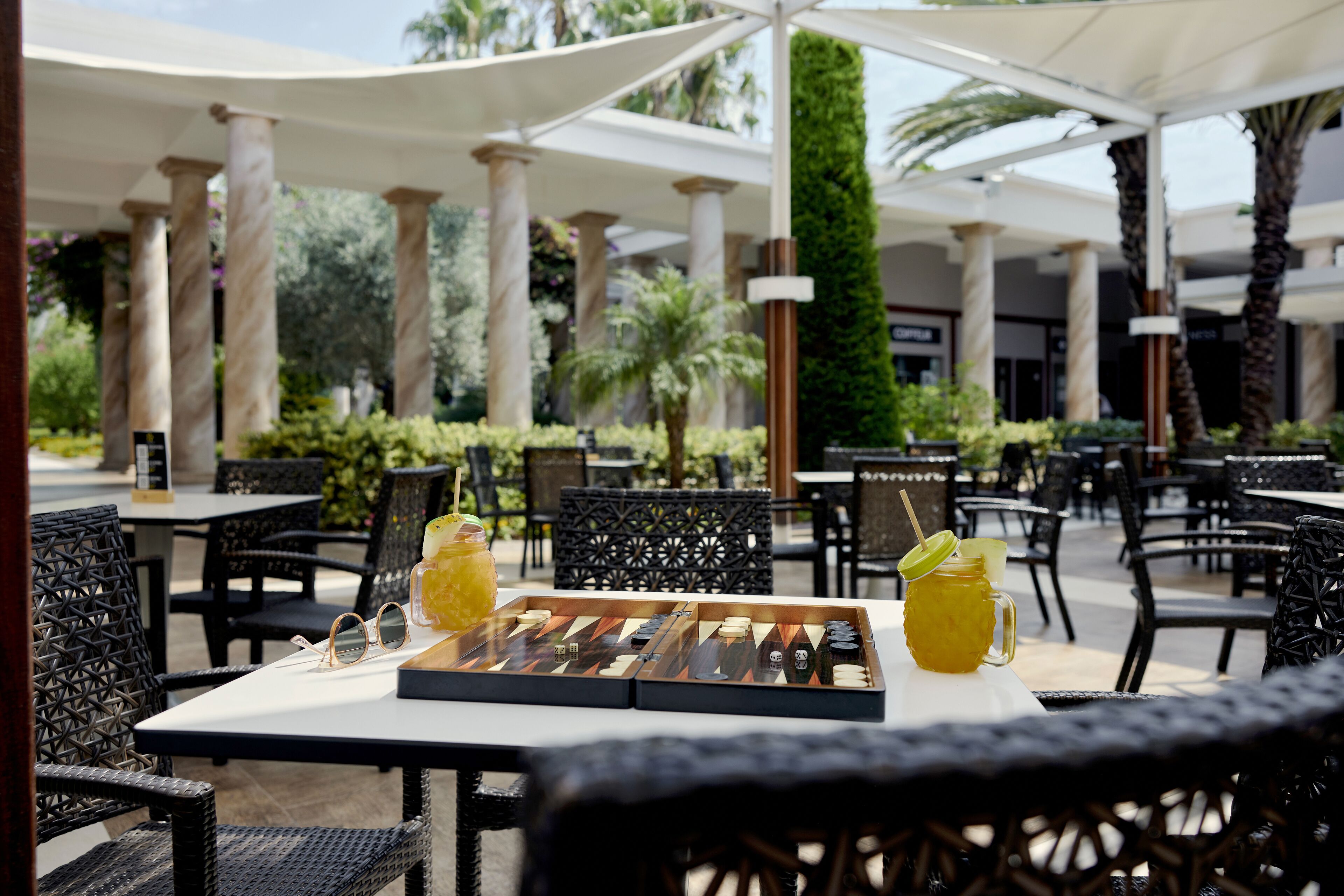 An outdoor dining area with tables and chairs, a chessboard, and a pitcher of lemonade.