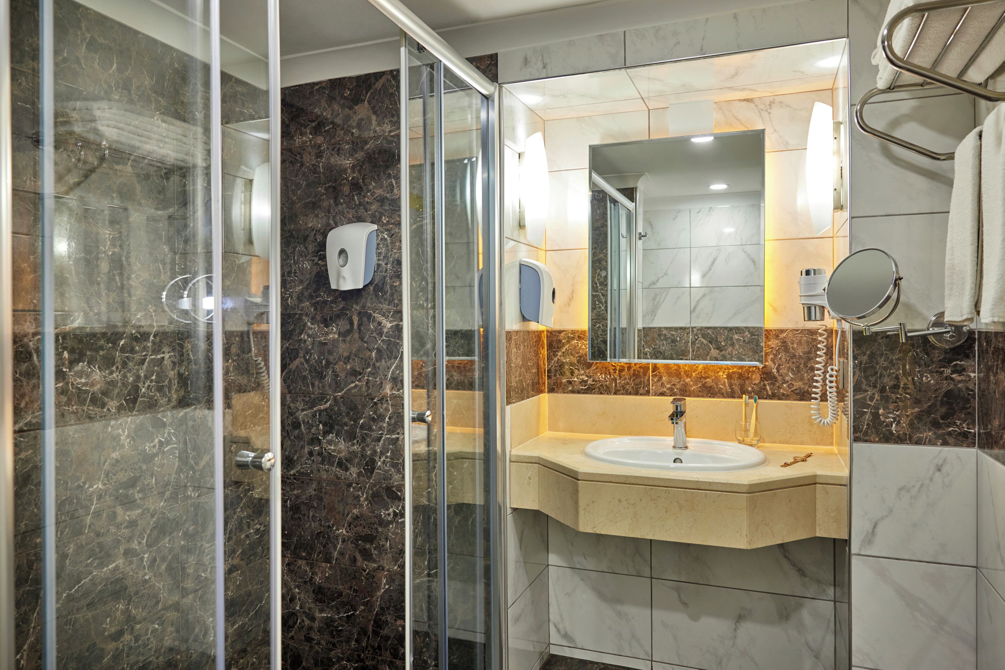 A modern bathroom with a glass shower enclosure, a sink with a marble countertop, and a mirror with a round frame.