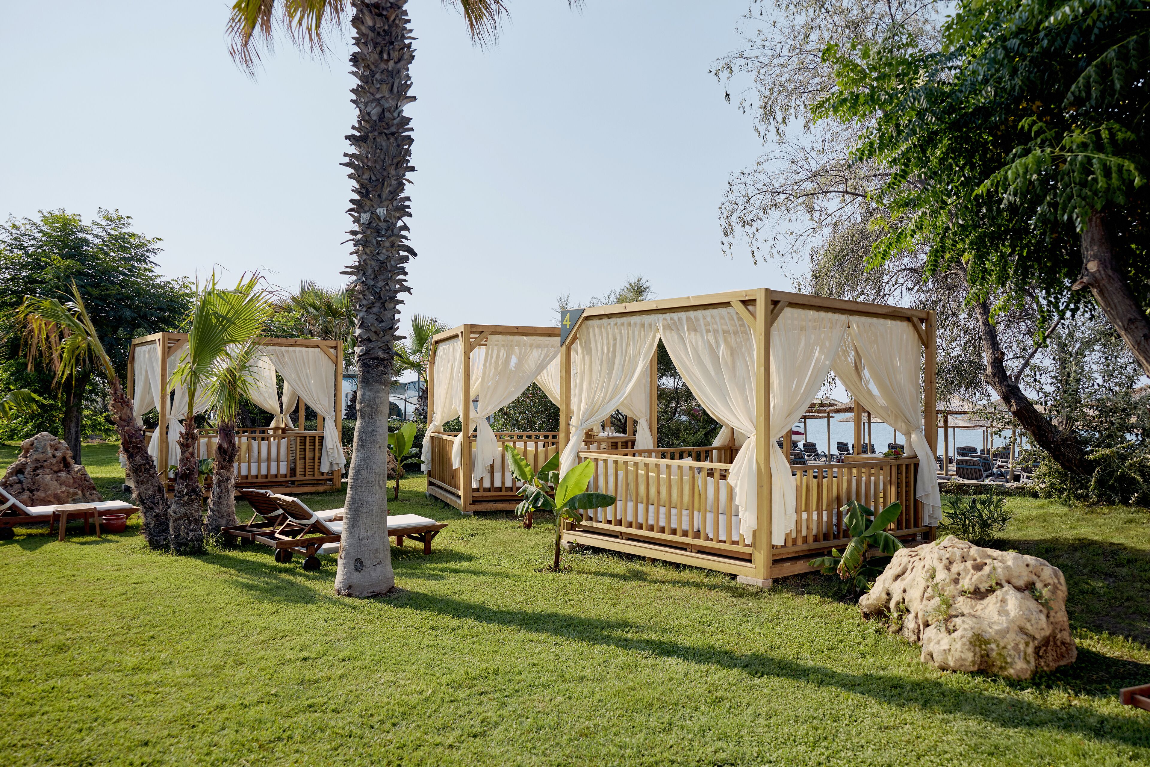A series of wooden gazebos with white canopies, surrounded by lush greenery and palm trees.