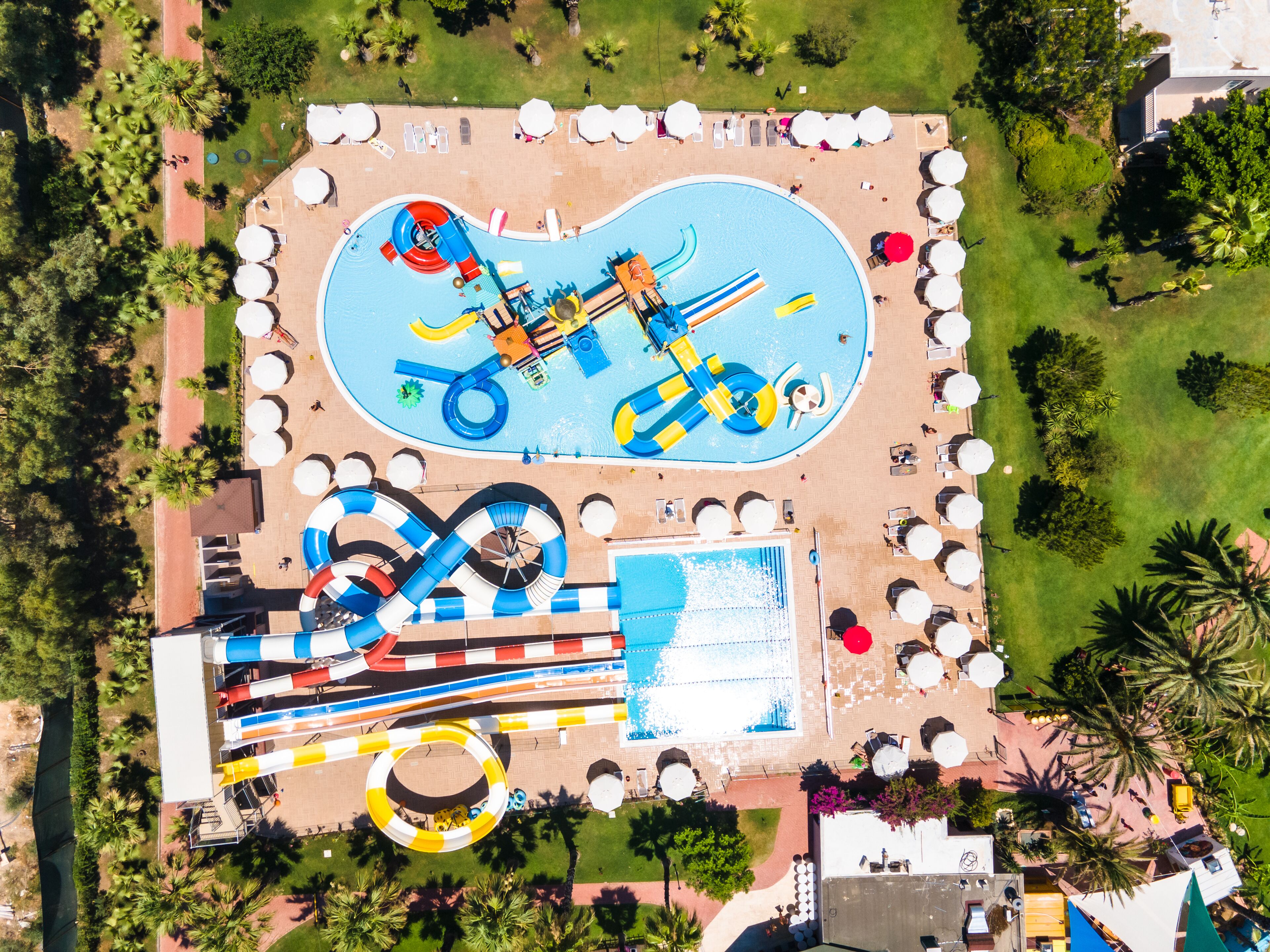Vista aérea de un parque acuático con piscina, toboganes y un río lento.