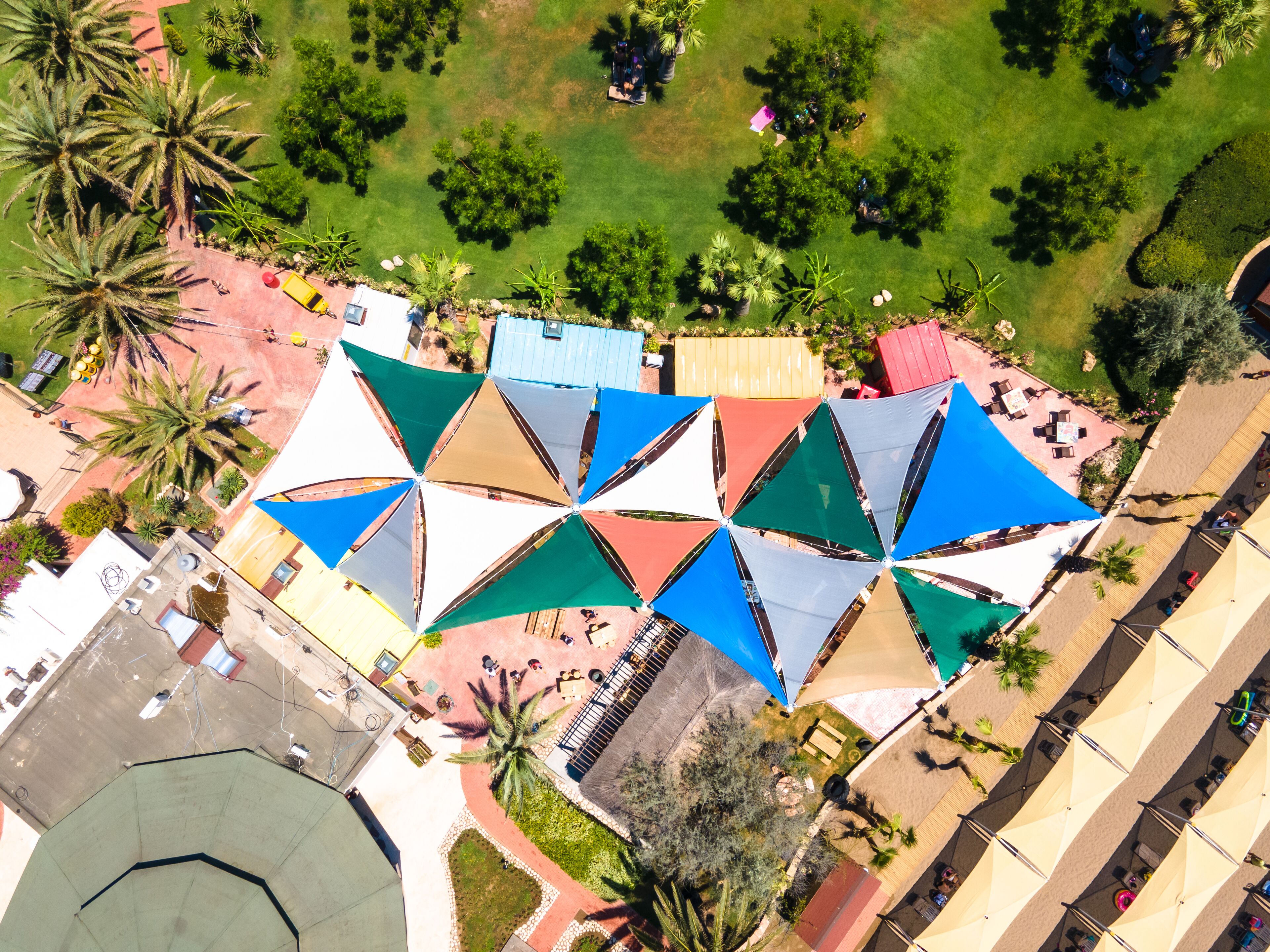 A rooftop terrace with multiple sunshades and seating areas, surrounded by greenery and palm trees.