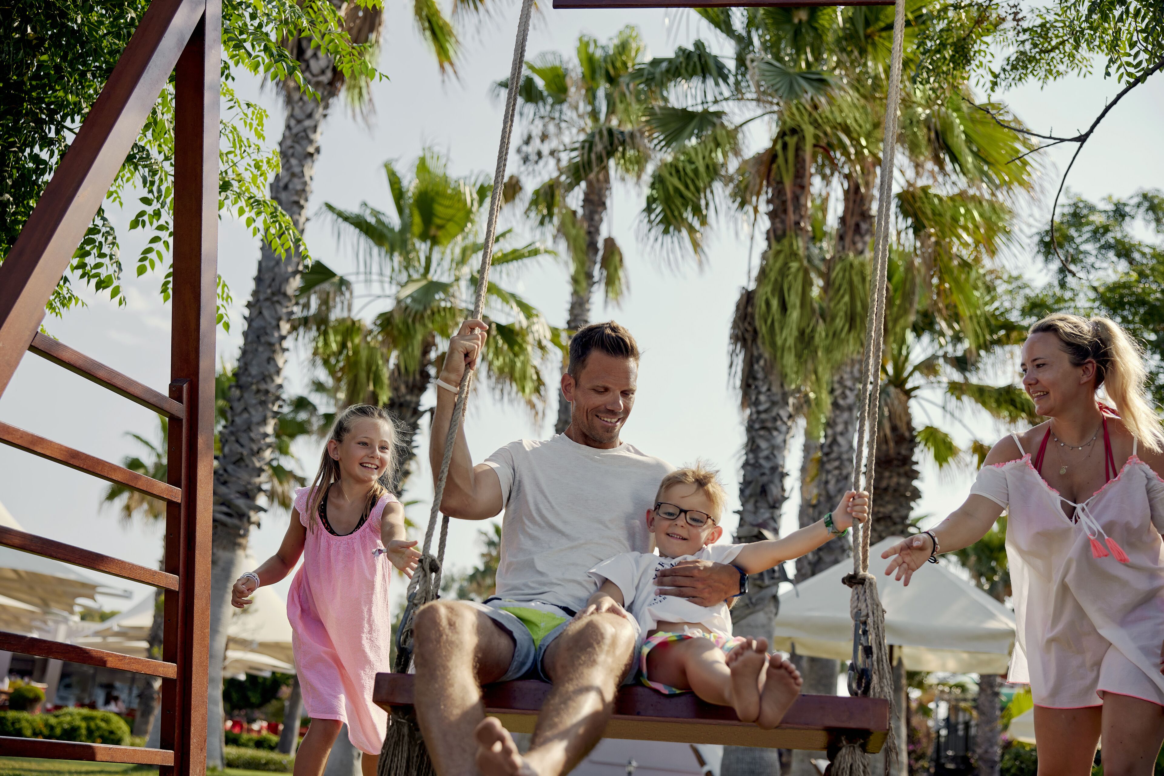 Una familia en un columpio con palmeras al fondo.