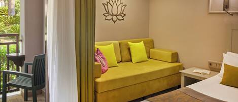 A hotel room with a yellow sofa, a bed, a nightstand, and a view of greenery outside.