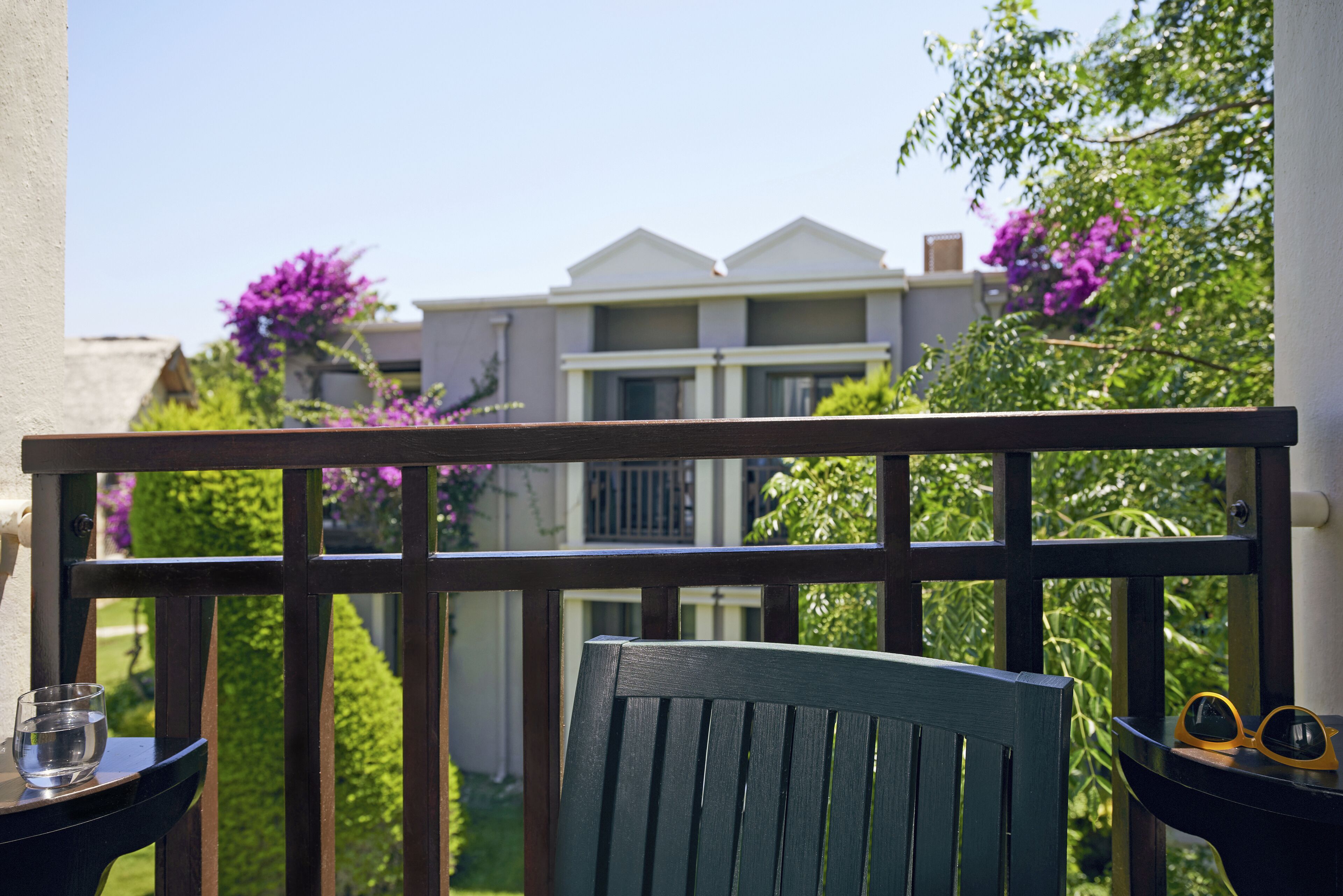 A balcony with a wooden railing, a green chair, and a table with a glass and sunglasses.