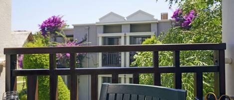 A balcony with a wooden railing, a green chair, and a table with a glass and sunglasses.
