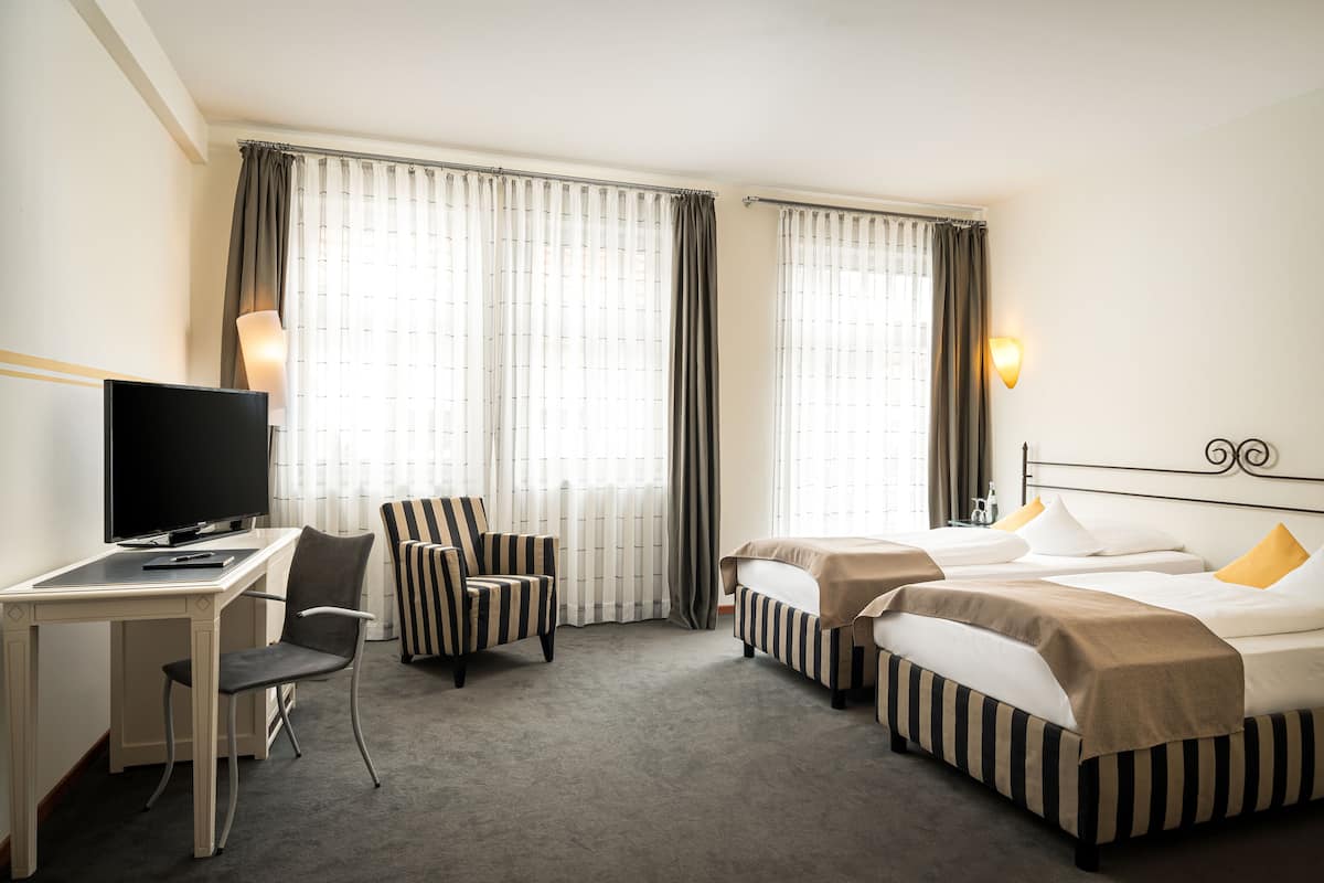 Une chambre d’hôtel avec un bureau, deux lits, une télévision et des rideaux.