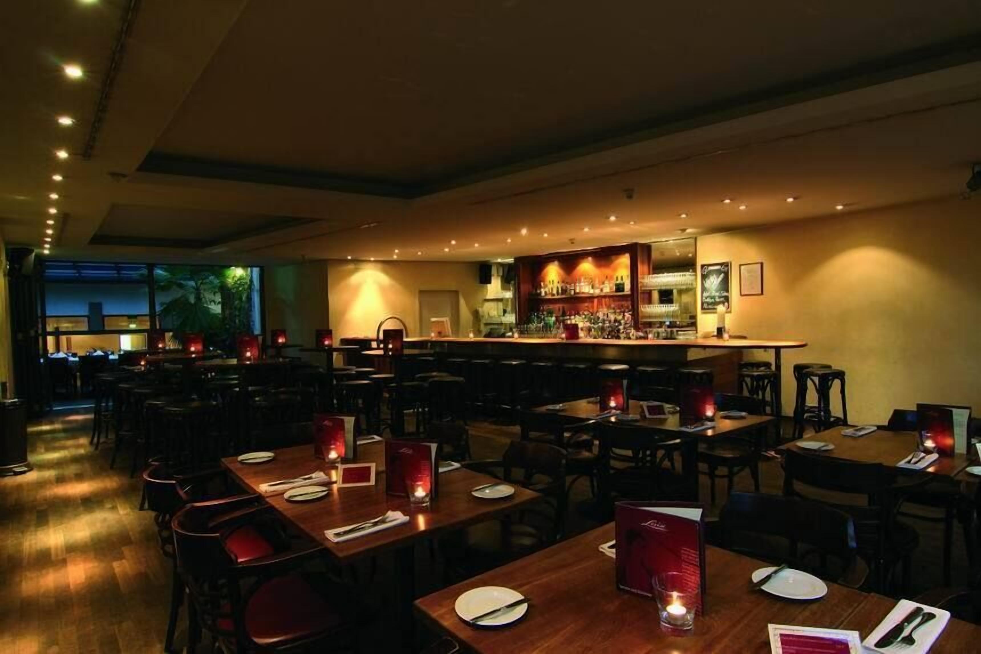 Un restaurante con varias mesas y sillas, una zona de bar y vistas al exterior.