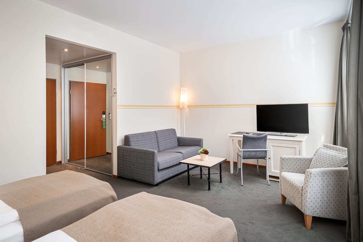 Une chambre d’hôtel avec un canapé, une petite table avec une plante, une télévision, un bureau et une chaise.