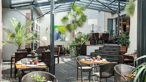 Un café en plein air avec des meubles en osier, des plantes en pot et un plafond en verre.