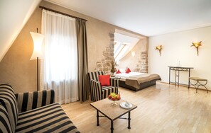 Ein modernes Hotelzimmer mit einem Bett, einem Sofa, einem kleinen Tisch mit Früchten, einer Lampe und Blick ins Freie.