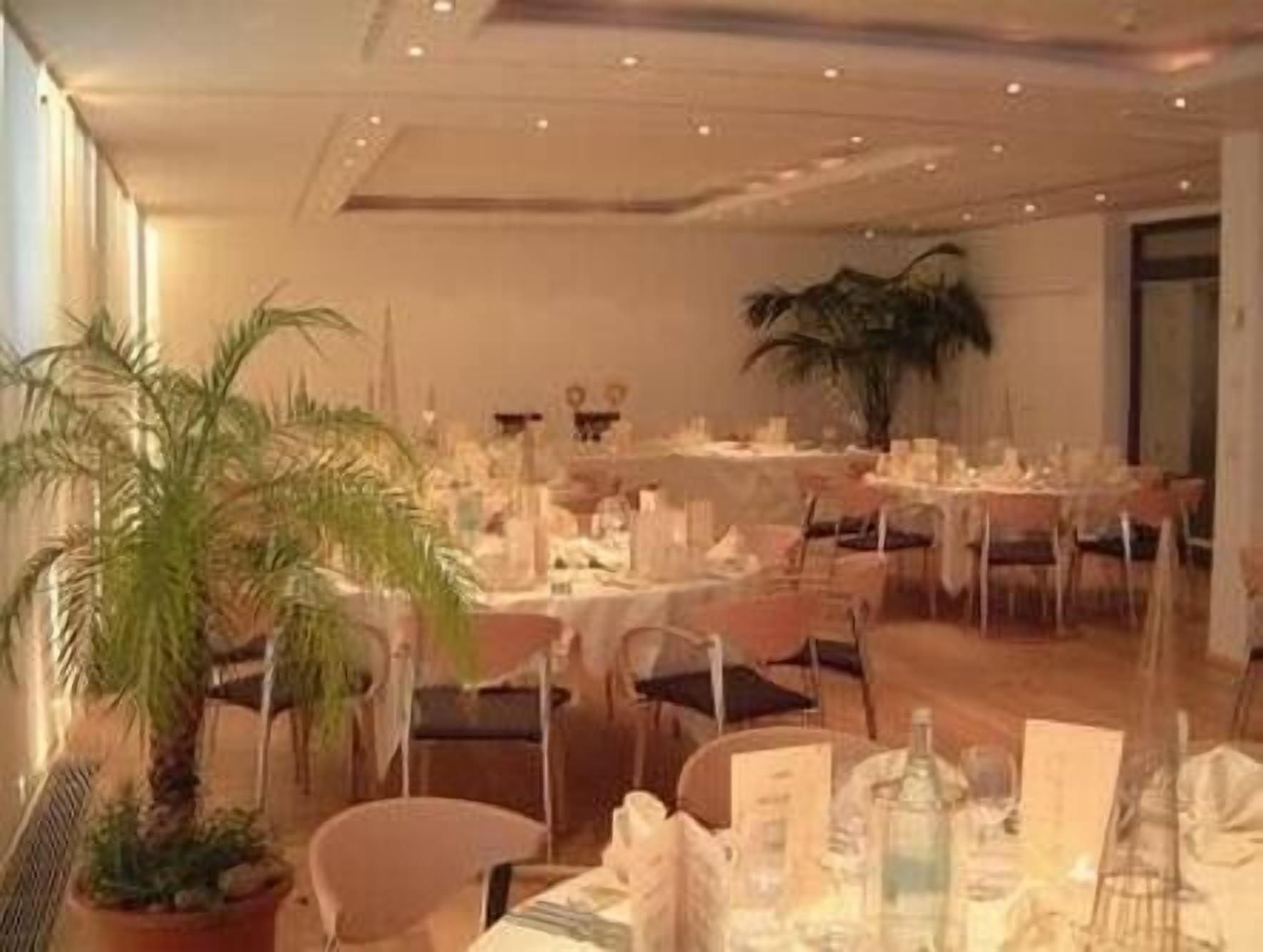 A banquet hall with round tables set for dining, chairs, and potted plants.