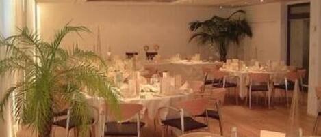 A banquet hall with round tables set for dining, chairs, and potted plants.