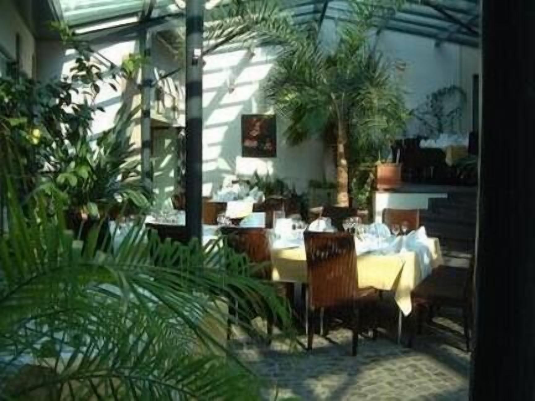 An outdoor dining area with tables and chairs, surrounded by greenery and a glass enclosure.