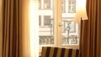 A room with a window, curtains, a lamp, and striped chairs.