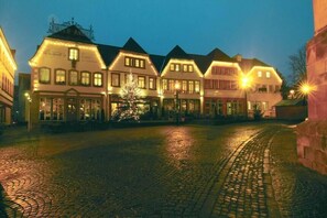 Eine Reihe traditioneller europäischer Gebäude mit beleuchteten Fassaden, eine Kopfsteinpflasterstraße und ein Weihnachtsbaum in der Mitte.