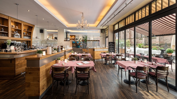 Un restaurant au décor intérieur en bois, avec des nappes à carreaux rouges et blancs, et une vue sur la rue grâce à de grandes fenêtres.