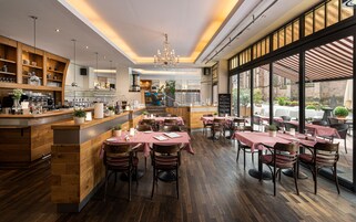 Un restaurante con interiores de madera, manteles a cuadros blancos y rojos, y vistas a la calle a través de amplias ventanas.