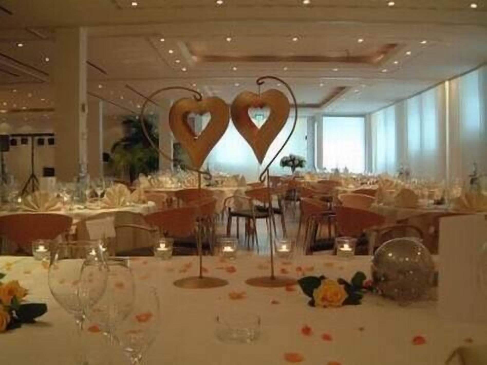 Salão de banquetes com mesas montadas para um evento formal, com decorações em formato de coração e centros de mesa com velas.
