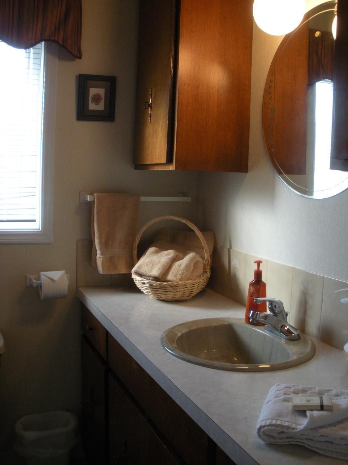 A bathroom with a sink, a mirror, a towel rack, a basket with towels, and a bottle of soap.