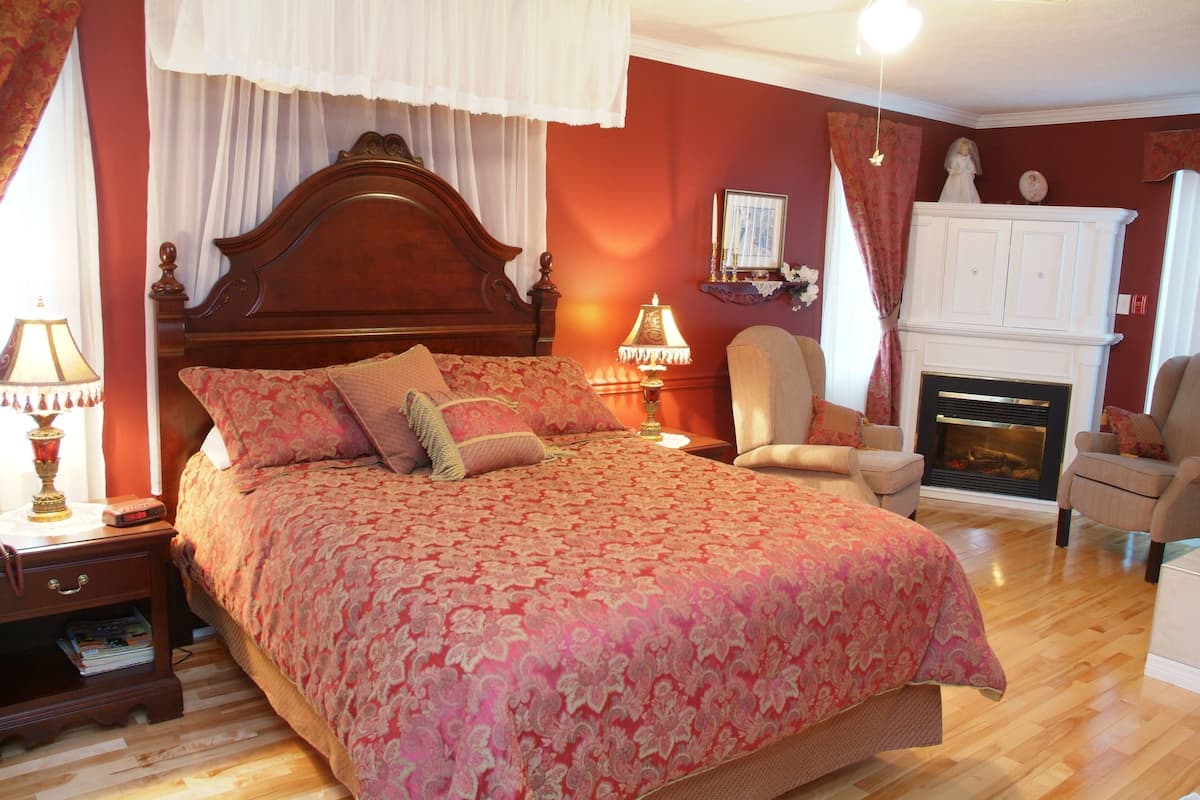 Un dormitorio con una cama grande, una mesita de noche, una silla, una chimenea y un espejo en la pared.