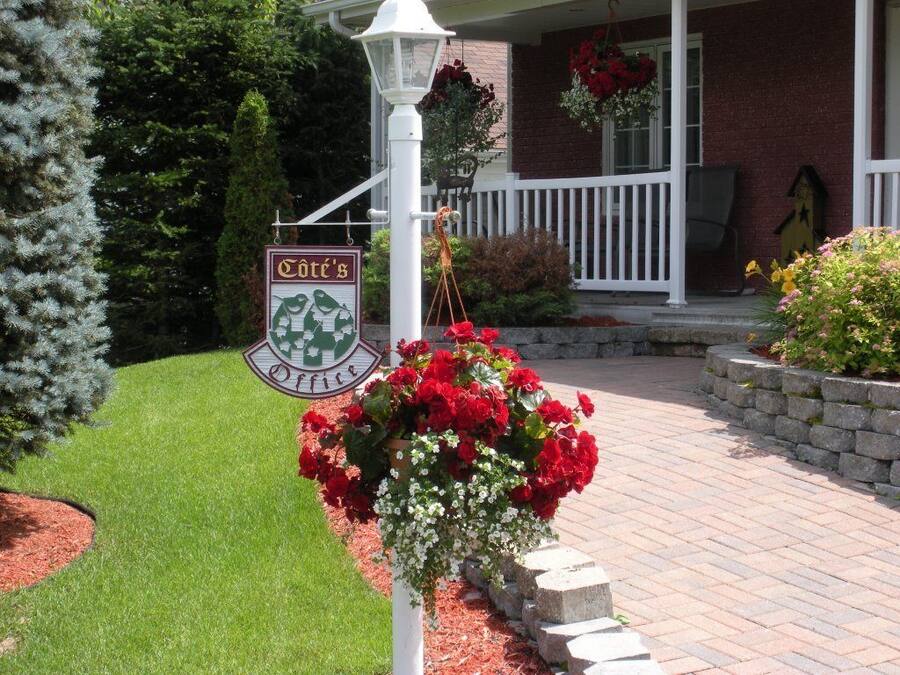 A porch with a sign reading "Côte's Office," surrounded by red flowers and a well-maintained lawn.
