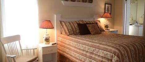 A bedroom with a bed, a rocking chair, a nightstand, and a shelf with decorative items.