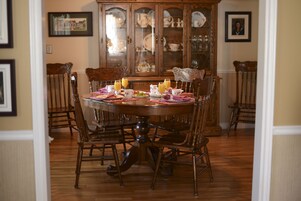 A dining room with a wooden table set for four, surrounded by matching chairs. A china cabinet with glass doors is in the background.