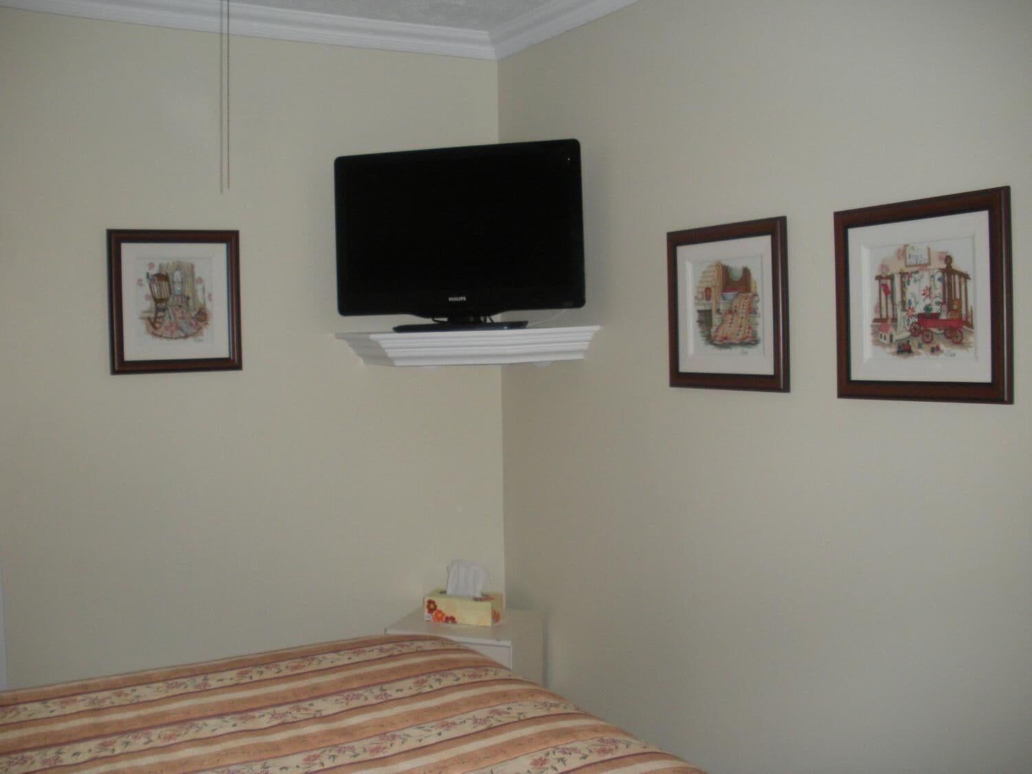 A hotel room with a bed, a television mounted on the wall, and three framed pictures on the wall.