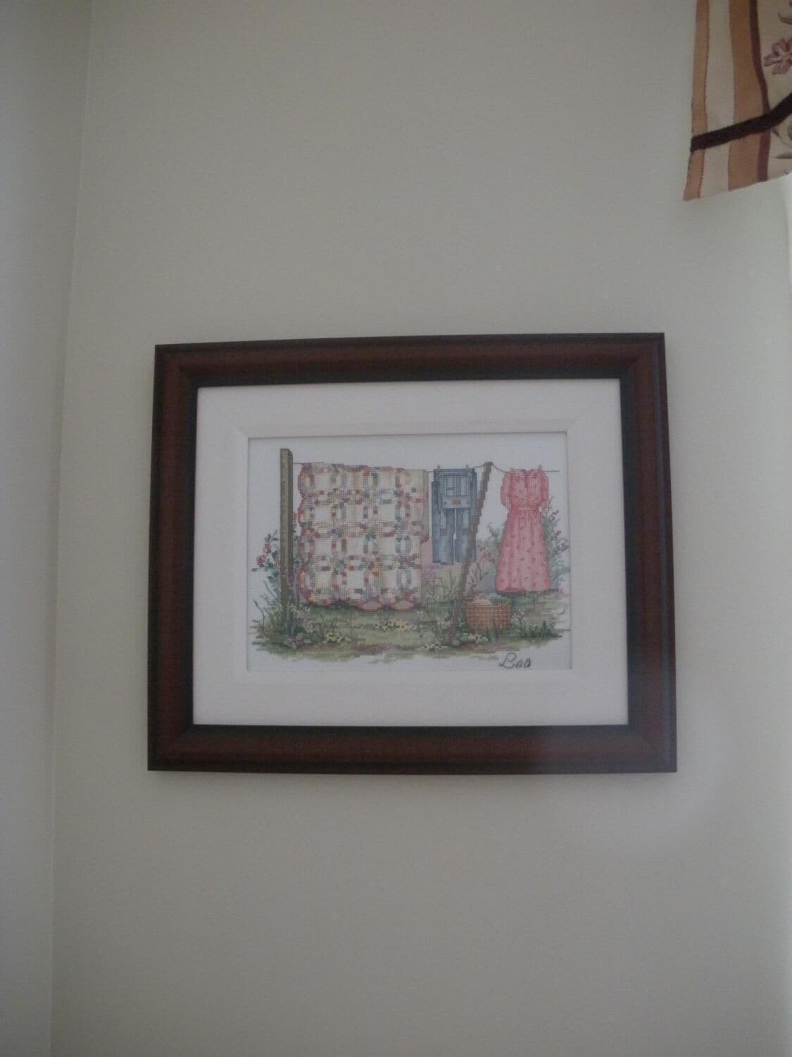 Une œuvre d’art encadrée représentant une maison avec une fenêtre et une robe rose.