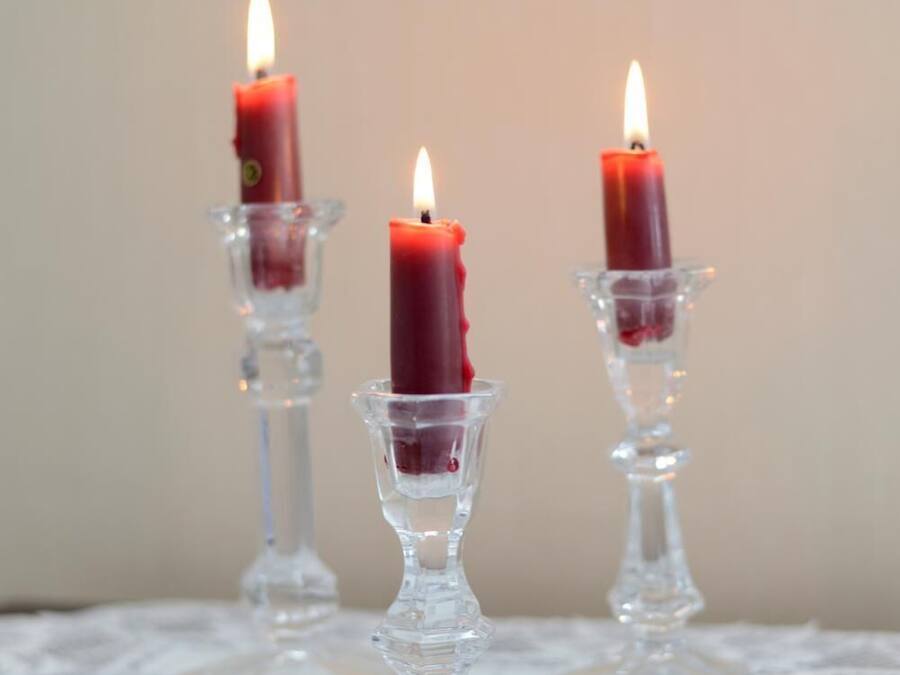 Three lit candles in glass holders on a lace tablecloth.