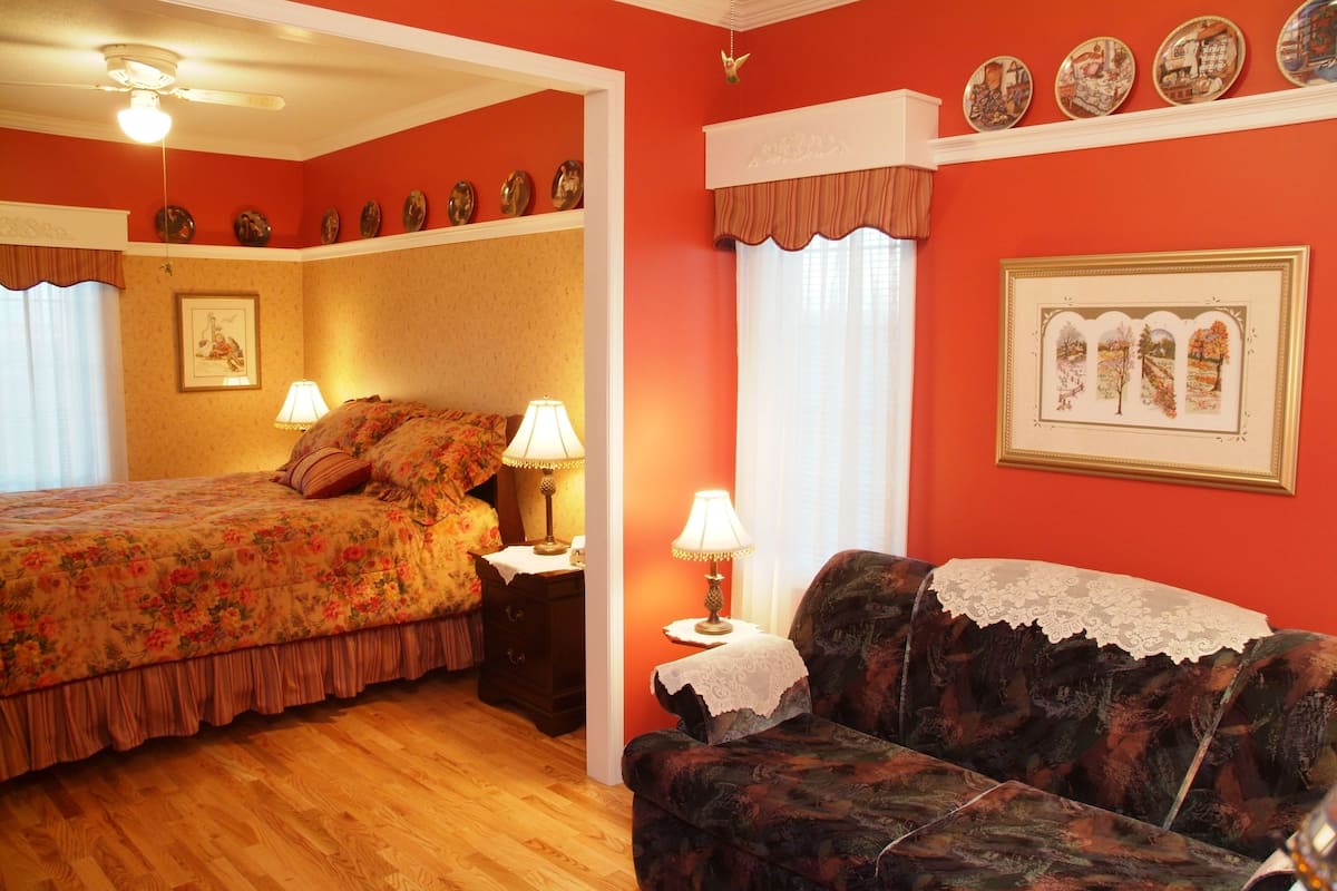 Un dormitorio con cama, mesita de noche, cómoda, sofá y ventana con cortinas.