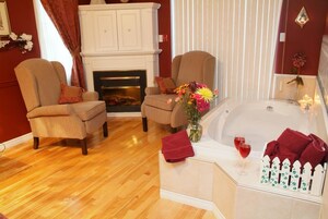 A room with two armchairs, a fireplace, a bathtub, and a vase of flowers.