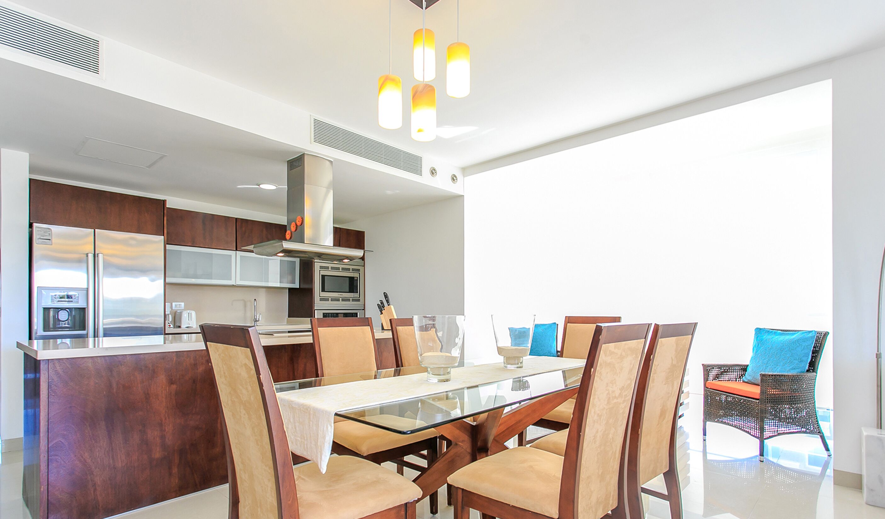 A modern kitchen with stainless steel appliances, a glass dining table, and wooden chairs.