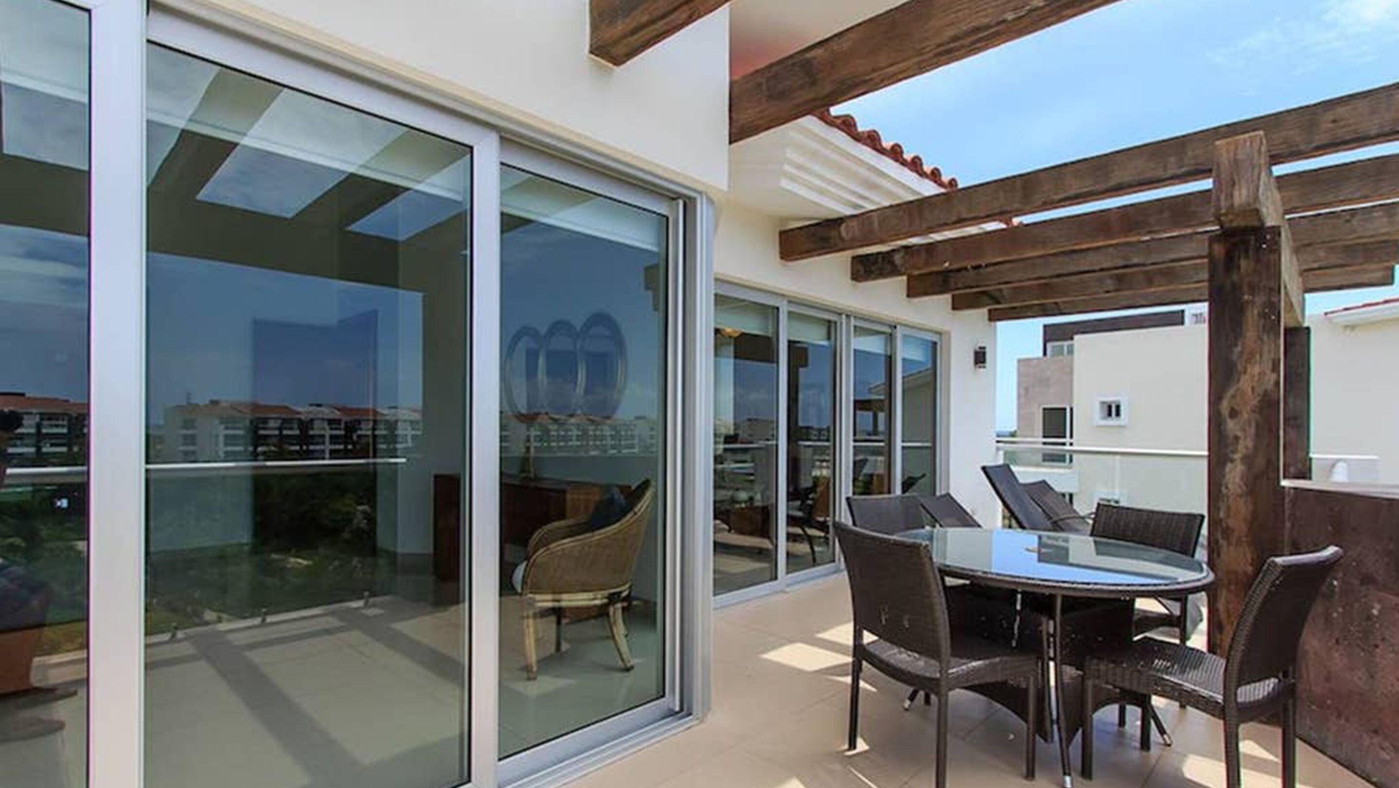Un patio exterior moderno con pared de vidrio, una mesa redonda y sillas.