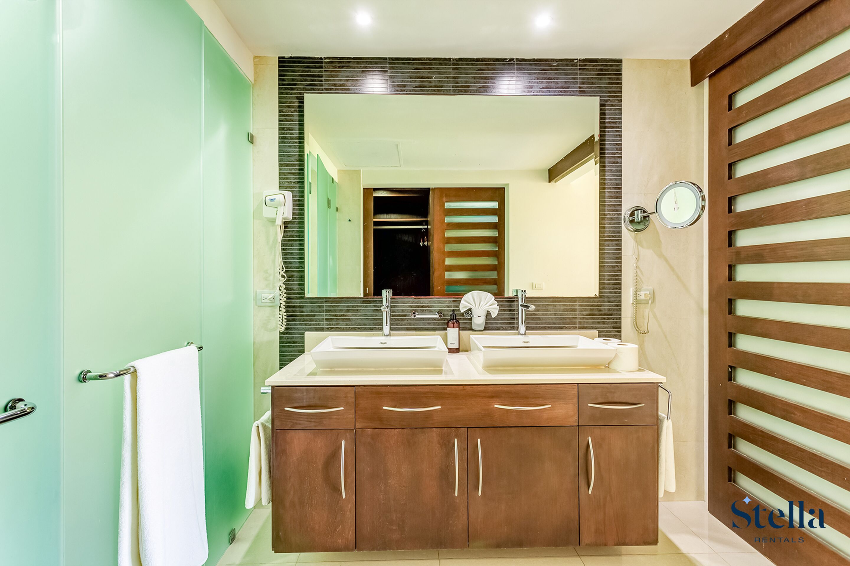 Une salle de bain avec un double vasque, des meubles en bois, un miroir et une horloge au mur.