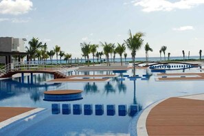 A swimming pool with a wooden deck, palm trees, and a view of the ocean. - Mareazul by Stella Rentals (Playa del Carmen)