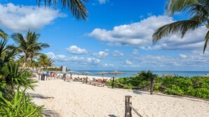 Ein Strand mit weißem Sand, Palmen und Sonnenschirmen.