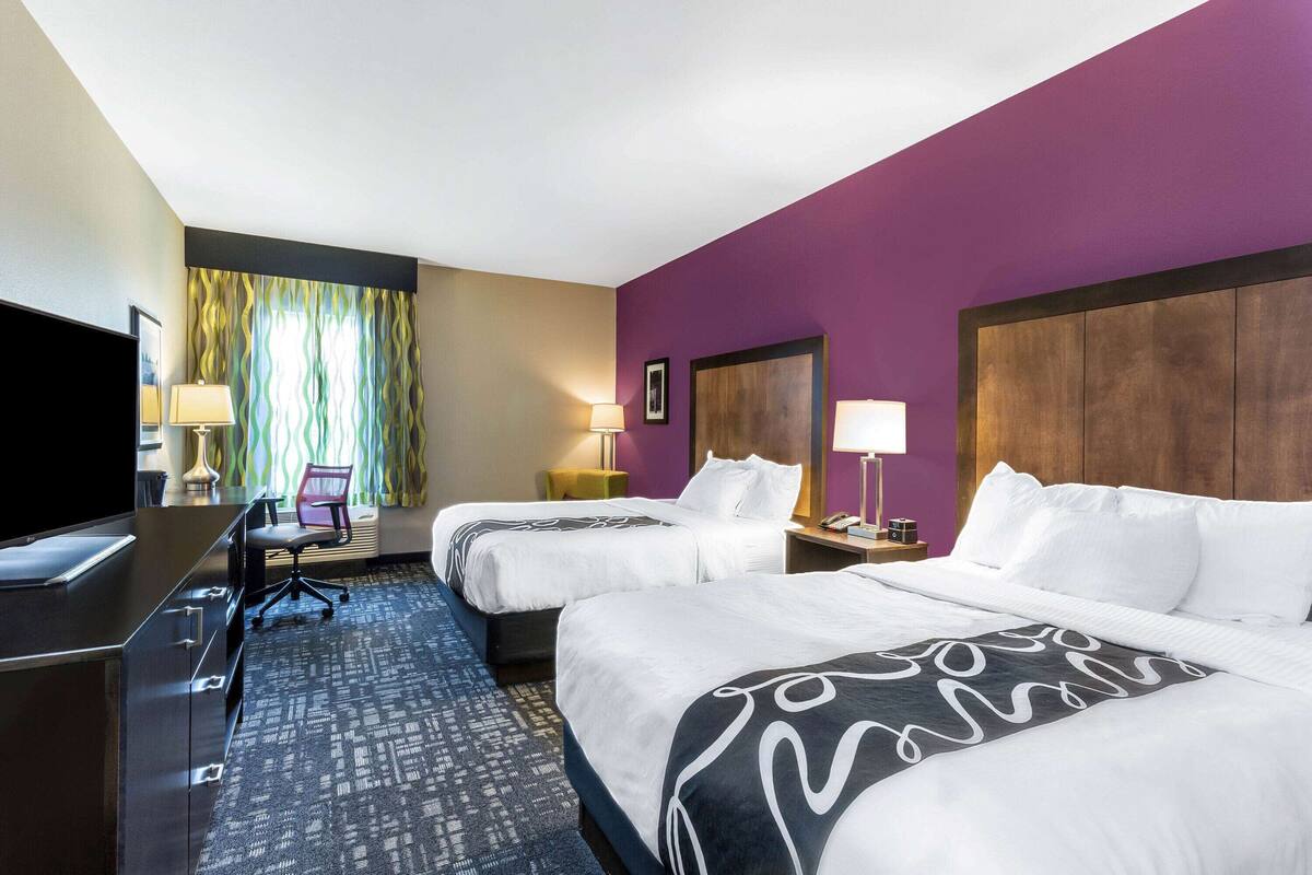 A hotel room with two beds, a desk, a TV, and a window with curtains.