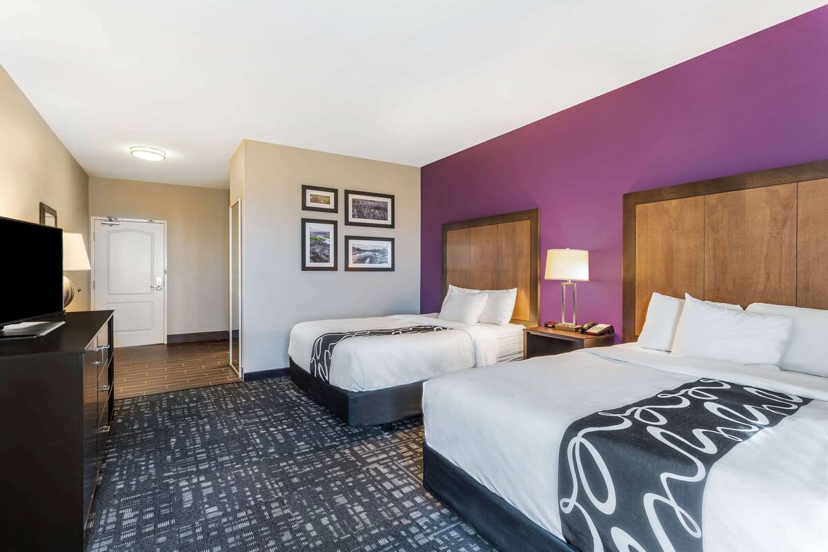 A hotel room with two beds, a TV, a desk, and a carpeted floor.